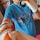 A person wearing a blue t-shirt with the words 'move smart' is holding a black-and-orange punching mitt and wearing boxing gloves. The background shows exercise equipment.