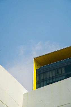 A sleek modern building with blue and yellow accents under a clear sky, reflecting minimalist design principles.