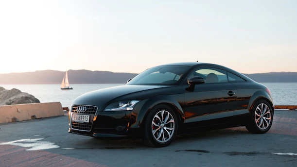 A sleek black sports car parked on a winding mountain road at sunset.
