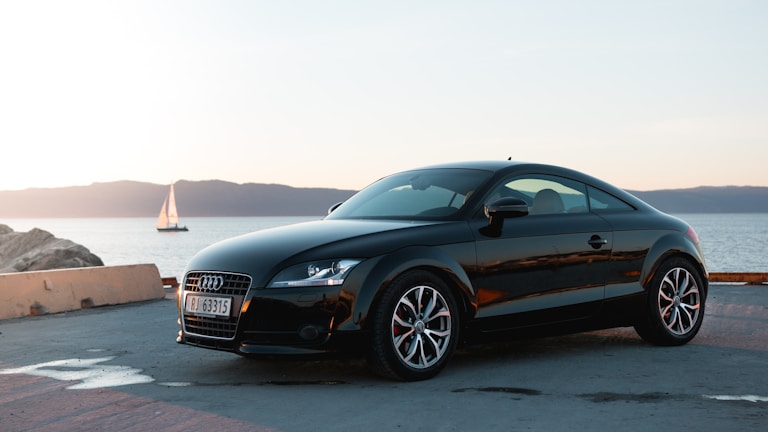 Sleek black luxury sports car parked on a coastal road at sunset.