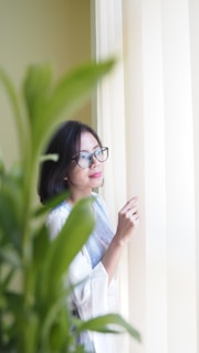 A thoughtful woman reflecting in a cozy, sunlit room filled with books and plants.
