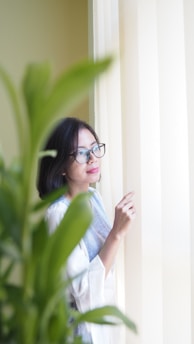 A thoughtful woman reflecting in a cozy, sunlit room filled with books and plants.
