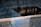 A square pool of water with a central void creates a calm and reflective ambiance. The surface of the water shimmers with a slight ripple effect, and there is a gentle play of shadows on the water. The edge of the pool features smooth stone with a light sheen.