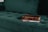A vintage book with a red-brown cover and a worn spine rests on top of a notebook with a spiral binding. These items are placed on a plush, dark green tufted couch.