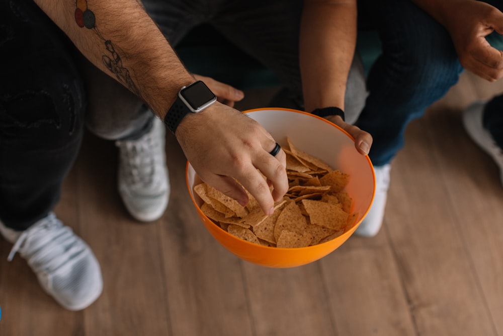 person holding orange bowl with potato chips