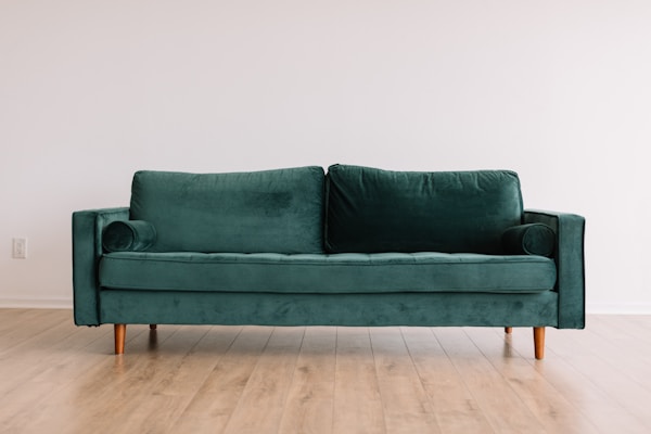 Cool hipster green couch sofa with brown wooden legs on wooden floorby Phillip Goldsberry