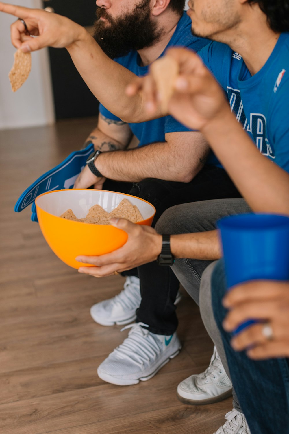파란색 NBA 댈러스 매버릭스 크루 넥 셔츠를 입은 사람이 감자 칩이 담긴 그릇을 들고 앉아 있습니다.