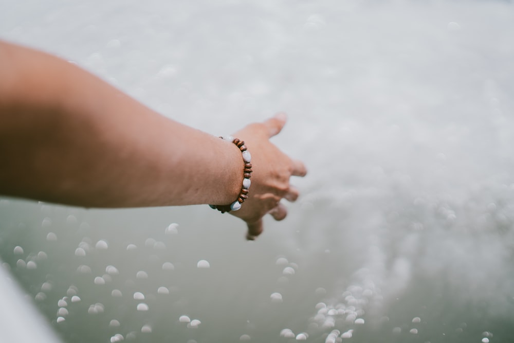 person wearing beaded brown-and-white bracelet touching splashing water