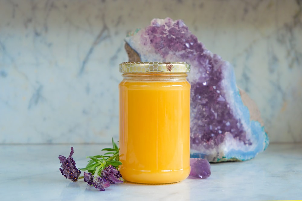 a jar of orange juice next to a purple flower