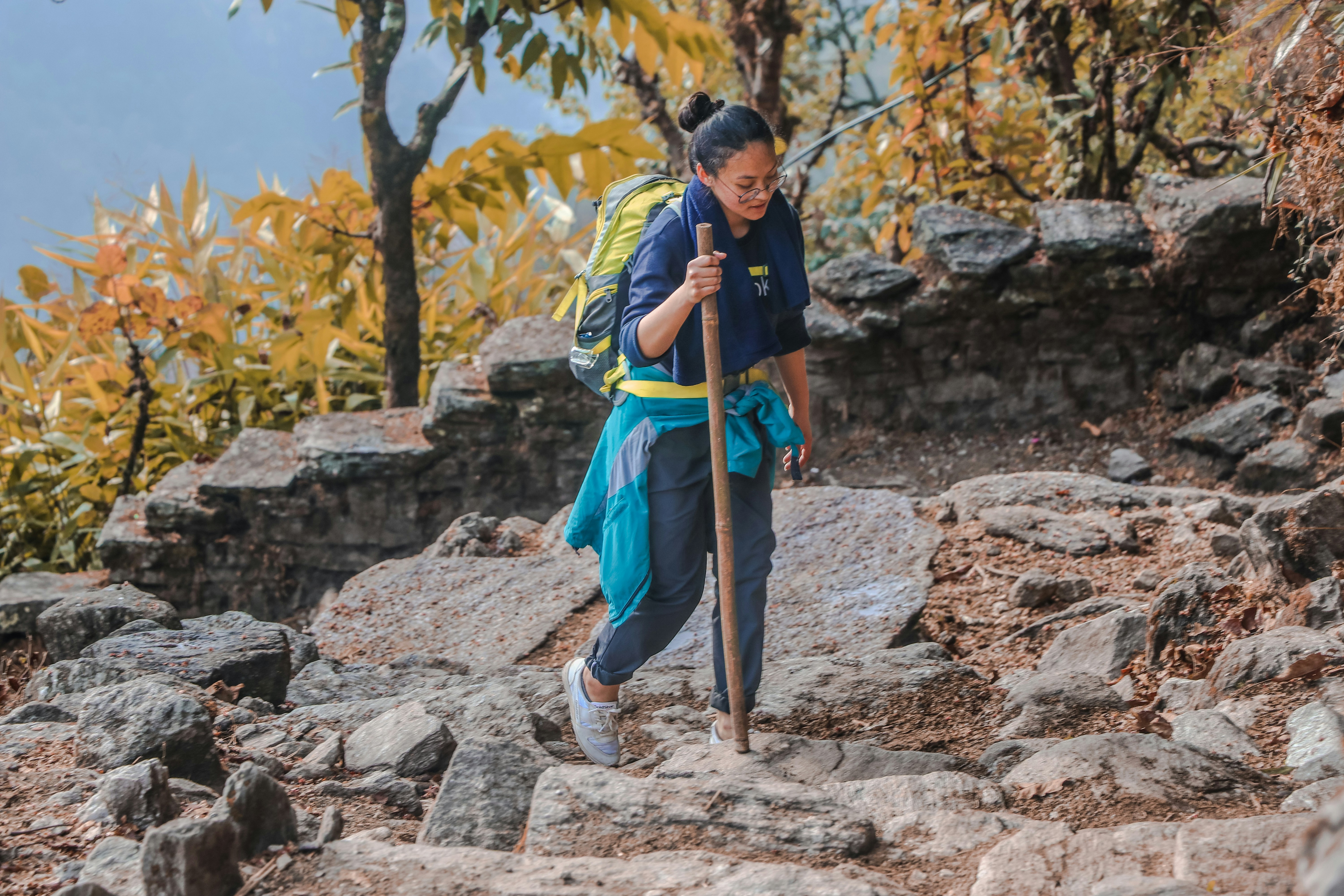 Woman trekking on mountain carrying backpack and wooden stick