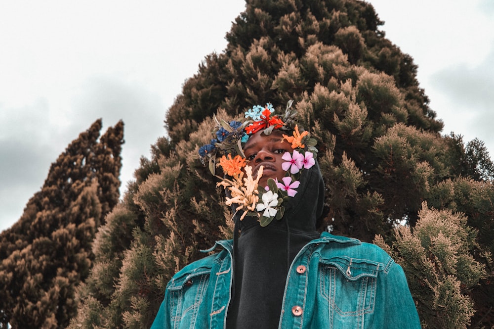 man standing with assorted-color flowers on his face near tall green tree