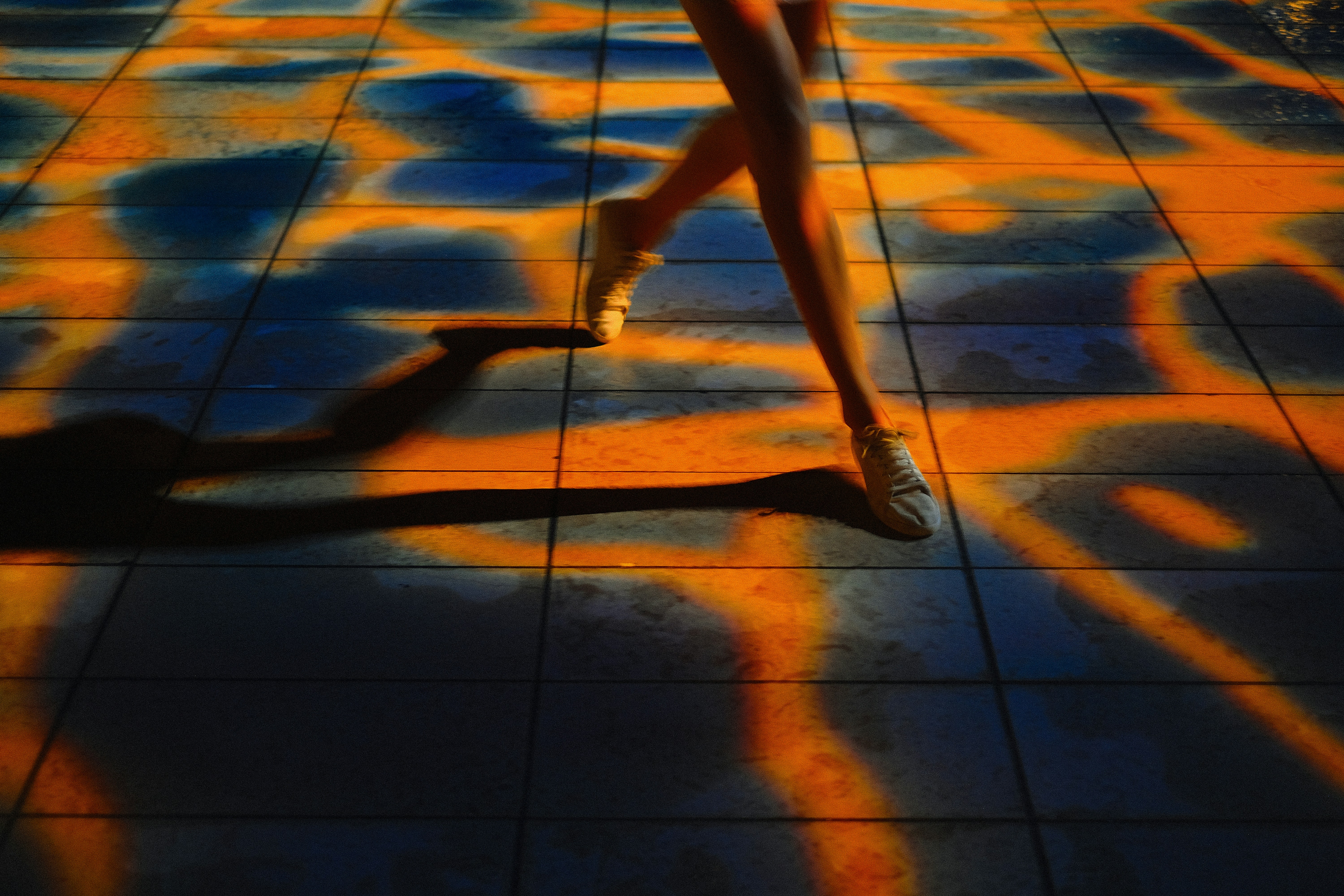 オレンジ色の影に包まれたタイルの床を歩く足。