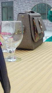 A close-up of a soft velvet handbag in deep burgundy resting on a rustic wooden table.