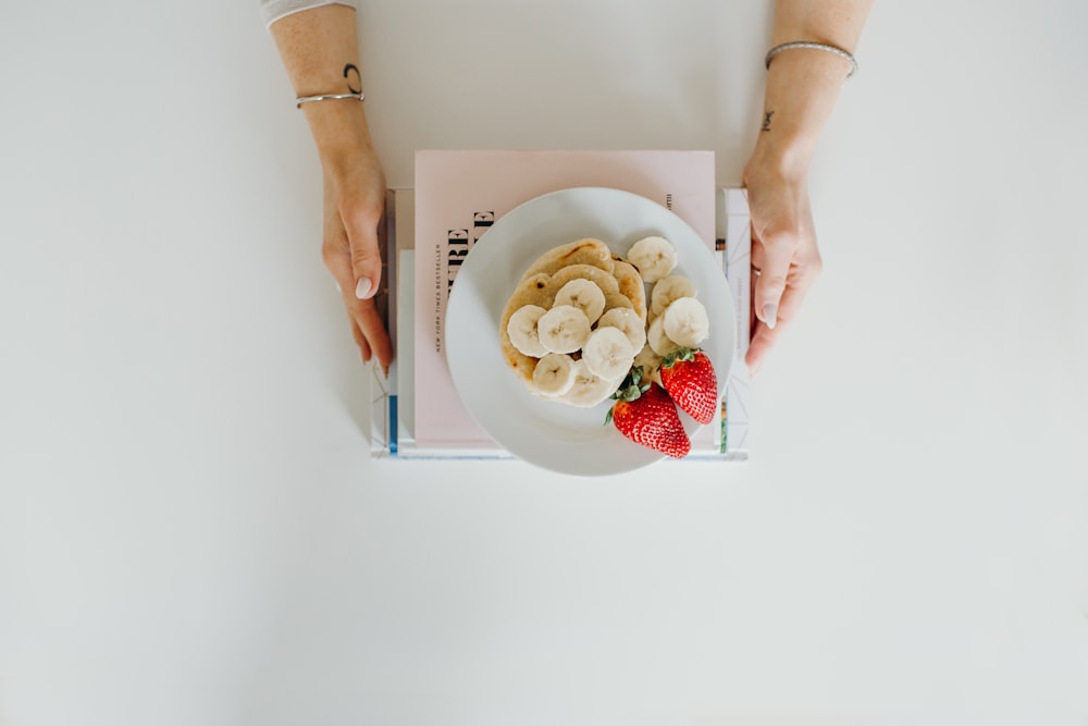 slices of banana fruit and two strawberries on table on top of books