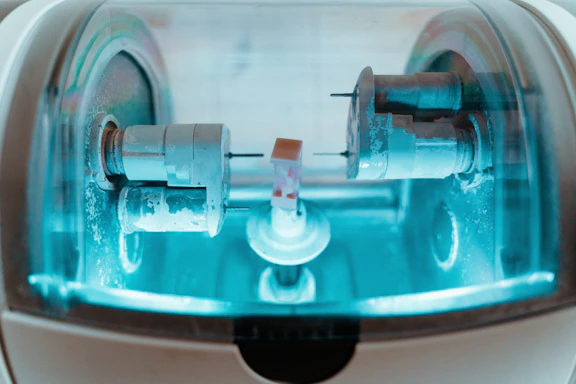 Close-up of a precision CNC milling machine cutting a complex metal part with blue accents in a clean industrial setting.