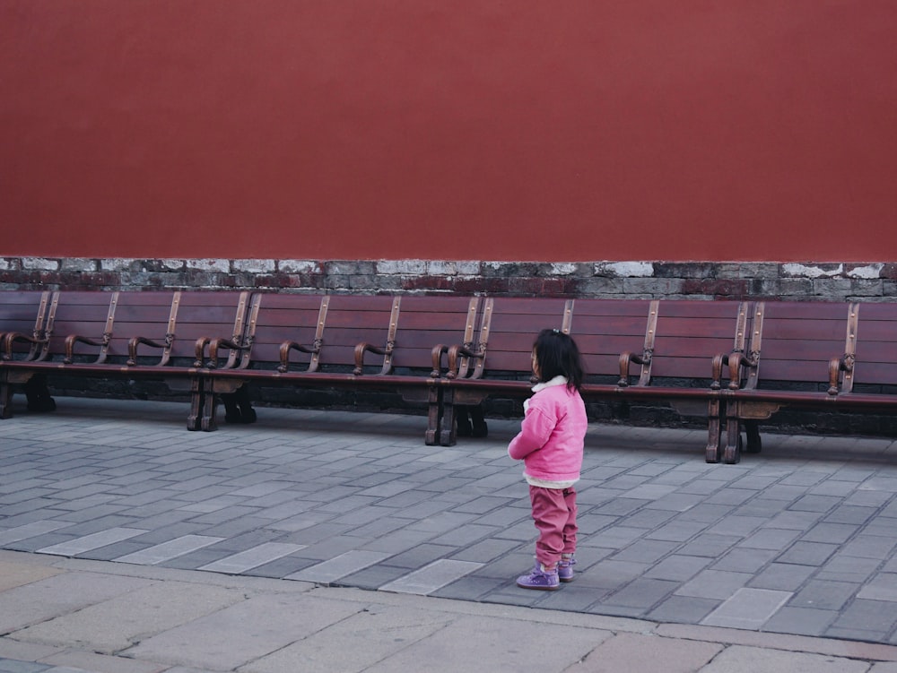 a little girl standing in front of a row of benches