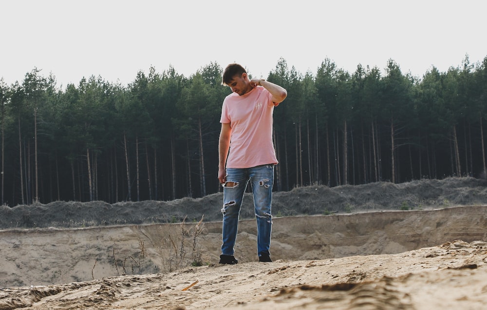 man in pink t-shirt and blue jeans standing on ground