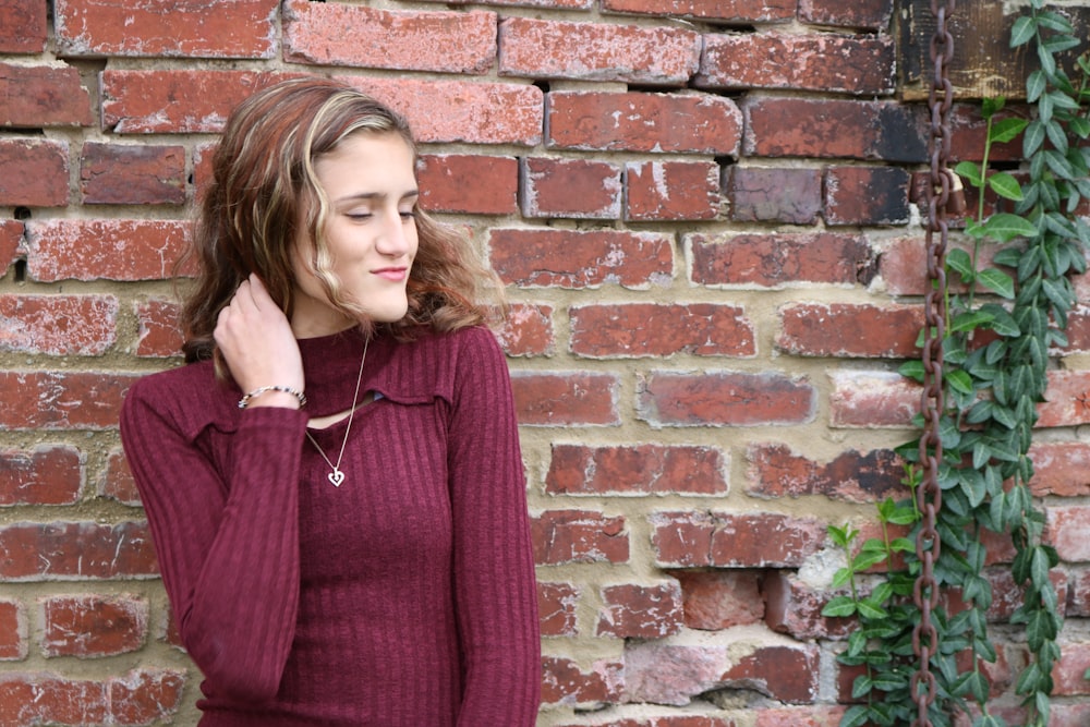 woman in purple sweater leaning against brick wall