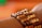 A close-up view of a wrist adorned with a bracelet made of wooden beads arranged in a patterned design. The beads are of varying shades of brown and tan, creating a textured and natural appearance. The background is softly blurred with warm tones of orange and green.