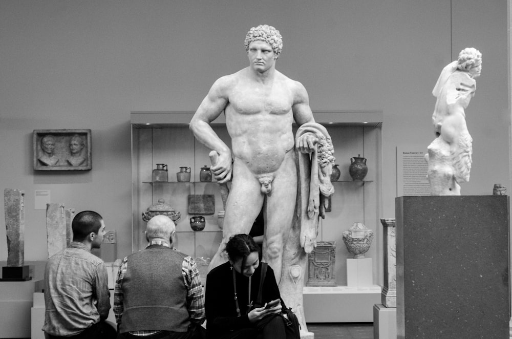 three people standing in front of naked man statue