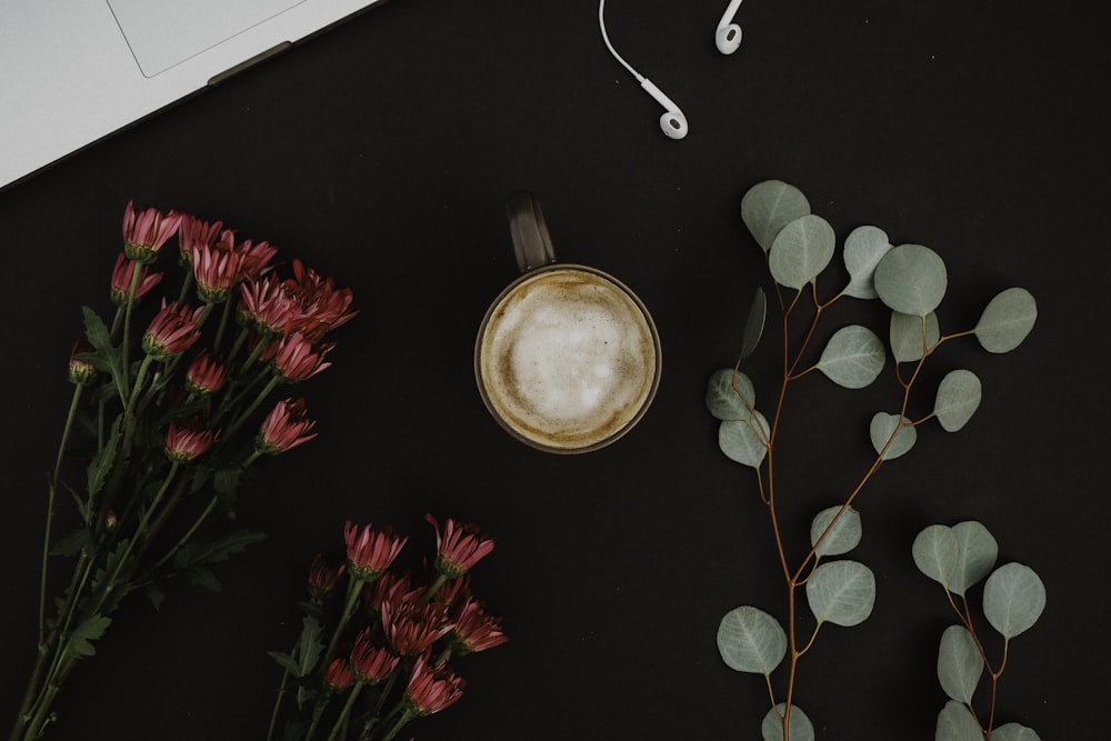 brown ceramic mug beside pink-petaled flowers on black surface