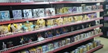 Shelves filled with various toy figurines and boxed sets, organized neatly. The figurines, mostly golden and shiny, depict various characters in dynamic poses. The boxed sets include colorful and detailed packaging featuring imagery of the characters. The overall arrangement is orderly, displaying a collection of collectibles.