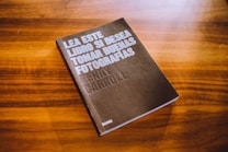 A book with a dark cover is placed on a wooden surface. The cover text reads 'Lea este libro si desea tomar buenas fotograf&iacute;as' by Henry Carroll. The background consists of a rich, warm wood grain texture.