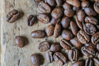 A collection of roasted coffee beans scattered on a wooden surface, showcasing their rich, dark brown color and glossy texture.