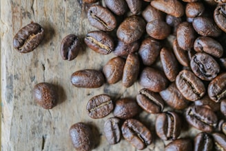 A collection of roasted coffee beans scattered on a wooden surface, showcasing their rich, dark brown color and glossy texture.