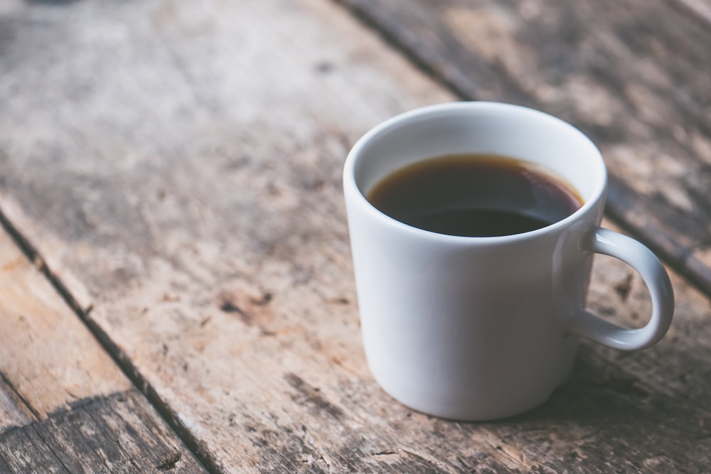 Kaffeegefüllter weißer Keramikbecher auf brauner Holzoberfläche