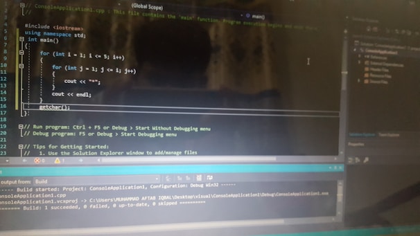 A computer screen displaying a code editor with a C++ program. The code includes a main function and nested for loops for printing stars. There are various sections of the interface visible, including a text editor with syntax highlighting, output panel showing build results, and project explorer on the side.