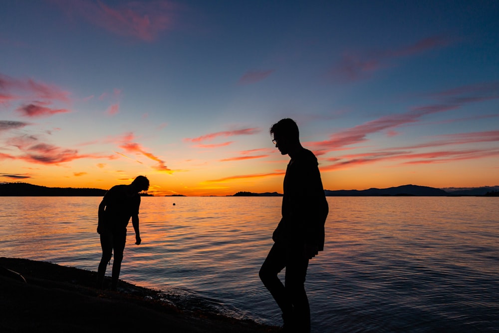 two men standing beside body of water