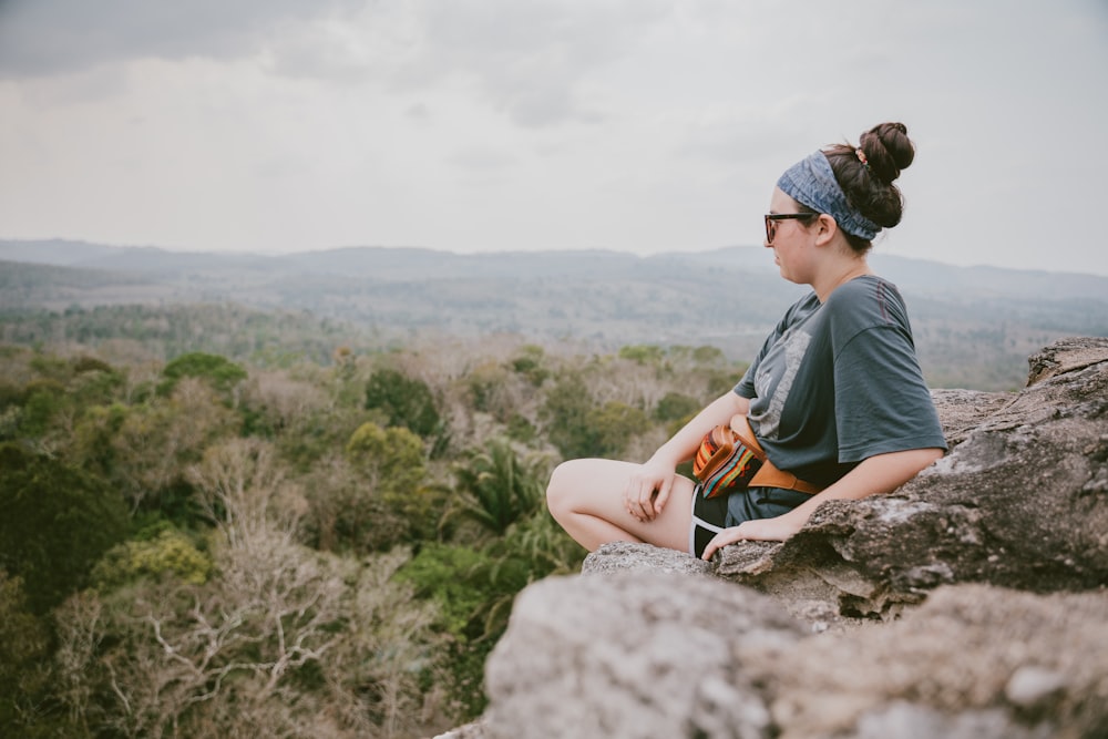 shallow focus photo of woman sitting on the edge of a cliff during daytime