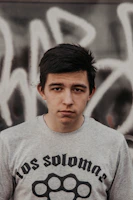 Young adult wearing a charcoal nisqala t-shirt standing against an urban graffiti wall.