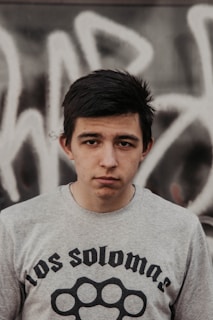 A young person wearing an oversized streetwear t-shirt standing against a graffiti wall.
