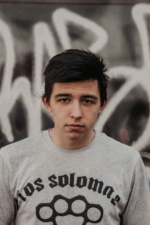 Young adult wearing a charcoal nisqala t-shirt standing against an urban graffiti wall.