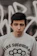 A confident young person wearing a black oversized graphic tee with bold white typography, standing against a gritty urban wall.