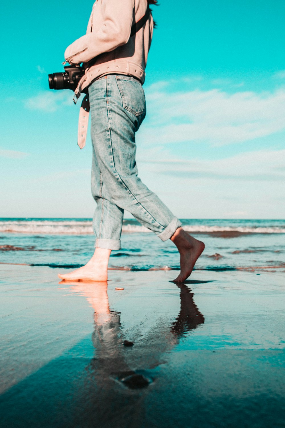 woman holding camera while walking on seashore