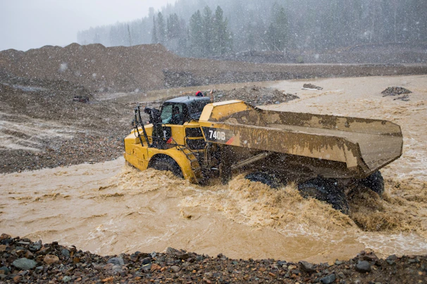 Heavy equipment working through a flooded street, removing mud and debris after severe flooding.
