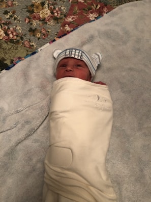 A baby wrapped in a soft cream blanket with subtle green sprout embroidery.