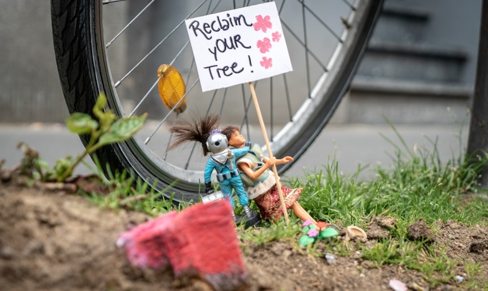 a small doll holding a sign next to a bike tire