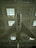 A vintage military jet airplane is suspended from the ceiling of a large indoor exhibition space. The aircraft has a sleek silver body with marked symbols on each wing, and it is viewed from below, emphasizing its aerodynamic shape and design features.