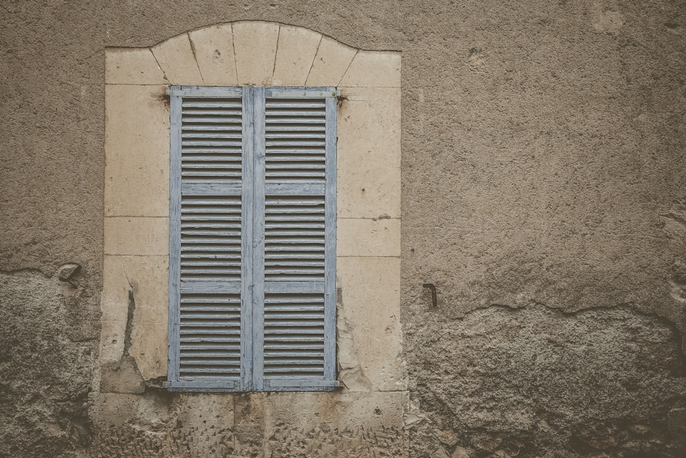 a window on a wall with a blue shutter