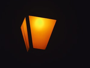 A glowing streetlamp emits a warm orange light, set against a dark backdrop. The geometric design features distinct angular panels, creating a modern aesthetic.