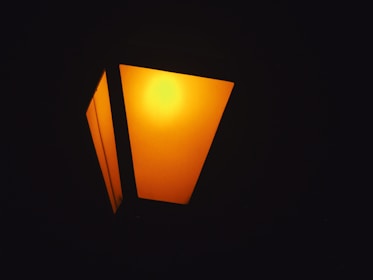 A glowing streetlamp emits a warm orange light, set against a dark backdrop. The geometric design features distinct angular panels, creating a modern aesthetic.