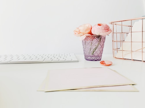 A soft pink and white minimalist workspace with a laptop and flowers.