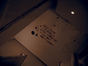 A wall is adorned with a motivational statement in bold black text. There are geometric line drawings and black ink splatter designs around the text. The scene is lit by a ceiling light, creating a modern and somewhat introspective atmosphere.