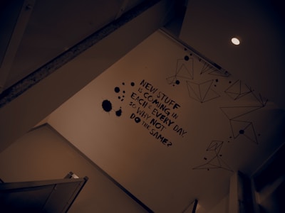 A wall is adorned with a motivational statement in bold black text. There are geometric line drawings and black ink splatter designs around the text. The scene is lit by a ceiling light, creating a modern and somewhat introspective atmosphere.