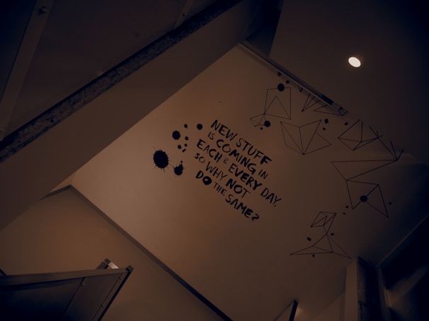 A wall is adorned with a motivational statement in bold black text. There are geometric line drawings and black ink splatter designs around the text. The scene is lit by a ceiling light, creating a modern and somewhat introspective atmosphere.