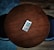 A smartphone displaying a colorful app interface lies at the center of a round wooden table. The dark wood grain contrasts with the bright phone screen. The table is surrounded by a couple of dark chairs positioned on a wooden floor.